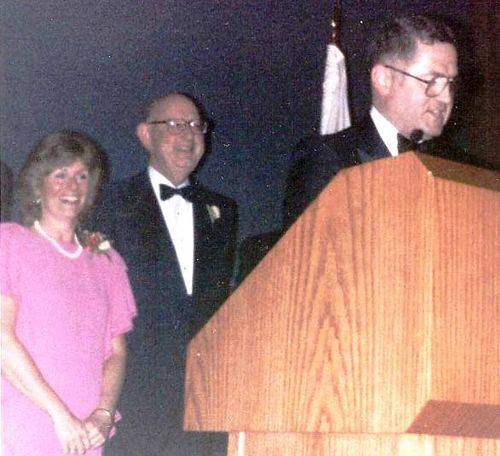 On Jan. 19, 1985, the Illinois State Society hosted its quadrennial nonpartisan Inaugural Gala at the National Press Club. Pictured at left is ISS officer Admiral Jim Carey, Chairman of the Maritme Commission, as he takes on master of ceremonies role at the 1985 Illinois State Society Inaugural Gala celebrating the second Inauguration of Illinois native President Ronald Reagan from Dixon. ISS board member Jeanne Jacob of Mendota is in back of the podium with another ISS officer.